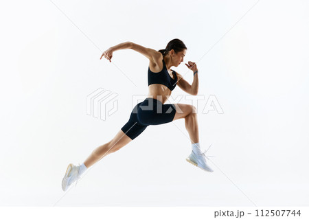 Dynamic image of young woman with strong, healthy, sportive body in sportswear in motion, training isolated over white studio background 112507744