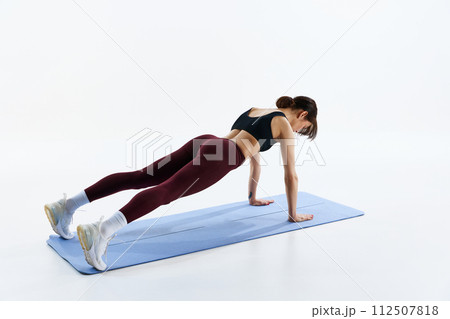 Sportive young woman in sportswear, with fit body training on fitness mat, standing in plank position isolated over white studio background Sportive young woman in sportswear, with fit body training on fitness mat, standing in plank position isolated over white studio background 112507818