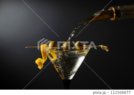 Classic dry martini cocktail with green olives and lemon peel on a black background. Classic dry martini cocktail with green olives and lemon peel on a black background. 112508877
