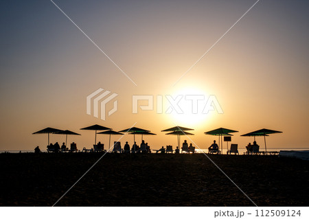 Silhouette of peoples and beach umbrella at the sunset in the sea 112509124