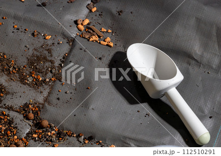 A white plastic scoop is on a grey surface with dirt and rocks 112510291