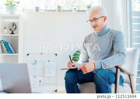 Professional Psychotherapy online. Middle aged male Psychologist having video call consultation on laptop while sitting on armchair In office. Specialist talking, counseling, helping patient online. Professional Psychotherapy online. Middle aged male Psychologist having video call consultation on laptop while sitting on armchair In office. Specialist talking, counseling, helping patient online. 112511684