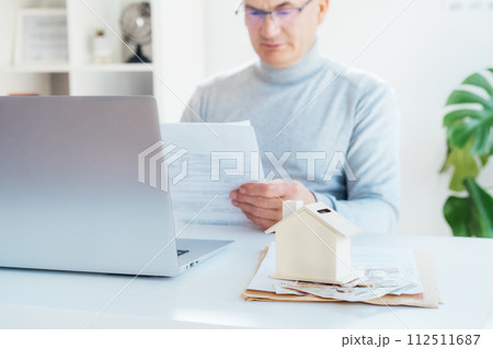 House model money box with cash on table and blurred man with docs works on laptop. Housing cost and payments. Real estate, property investment. Home mortgage loan rate. Saving money for retirement. House model money box with cash on table and blurred man with docs works on laptop. Housing cost and payments. Real estate, property investment. Home mortgage loan rate. Saving money for retirement. 112511687