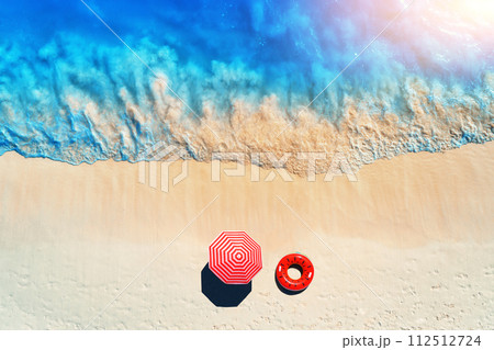 Aerial view of blue sea, sandy beach with red swim ring, umbrella 112512724