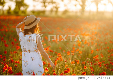 Beautiful girl in the poppy field at sunset in a white dress and hat. Beautiful girl in the poppy field at sunset in a white dress and hat. 112514553