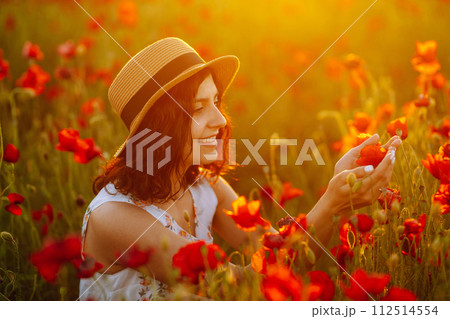 Beautiful girl in the poppy field at sunset in a white dress and hat. 112514554