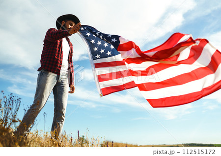 4th of July. American Flag. Traveler with the flag of America. The man in a hat, a backpack, a shirt and jeans. 112515172