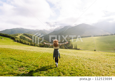 Woman walking on through green grass valley on background big mountains. Resting concept. 112515694