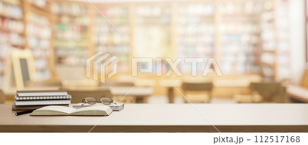 A wooden table features eyeglasses, books, and a presentation space in a school library. 112517168