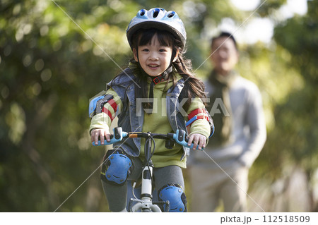 little asian girl riding bike outdoors in city park 112518509