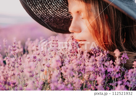 Woman lavender field. Happy carefree woman in black dress and hat with large brim smelling a blooming lavender on sunset. Perfect for inspirational and warm concepts in travel and wanderlust. Close up Woman lavender field. Happy carefree woman in black dress and hat with large brim smelling a blooming lavender on sunset. Perfect for inspirational and warm concepts in travel and wanderlust. Close up 112521932