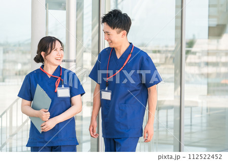 病院の通路で話す医者・医師・看護師・医療従事者・ドクター・作業療法士・理学療法士の男女 112522452