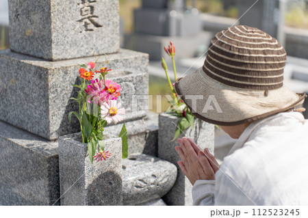 墓前で手を合わせて墓参りするシニア女性 墓前で手を合わせて墓参りするシニア女性 112523245