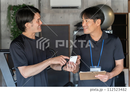 パーソナルトレーニングでカウンセリングを受ける若いアジア人男性とパーソナルトレーナーの男性 パーソナルトレーニングでカウンセリングを受ける若いアジア人男性とパーソナルトレーナーの男性 112523482