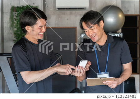 パーソナルトレーニングでカウンセリングを受ける若いアジア人男性とパーソナルトレーナーの男性 パーソナルトレーニングでカウンセリングを受ける若いアジア人男性とパーソナルトレーナーの男性 112523483
