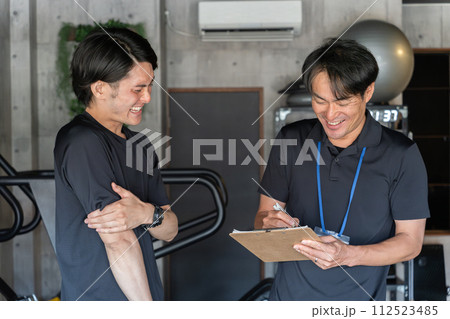 パーソナルトレーニングのカウンセリングで会員男性の悩みを聞くパーソナルトレーナーの男性 112523485