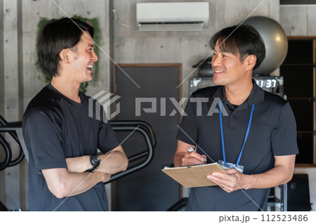 パーソナルジムで会員男性にカウンセリングするパーソナルトレーナーの男性 112523486