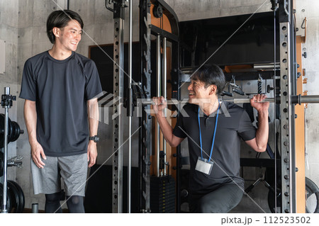 パーソナルジムで会員にトレーニングの見本を見せる男性トレーナー（スクワット・ブルガリアンスクワット 112523502