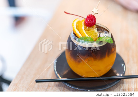 Iced Black americano Orange Coffee topping with mint leaves and sliced in a glass on wooden background in coffee shop cafe. 112523584