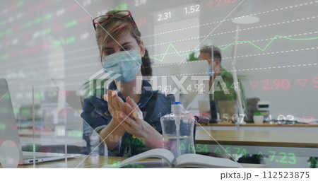 Image of digital interface showing statistics with colleagues in office wearing face masks 112523875
