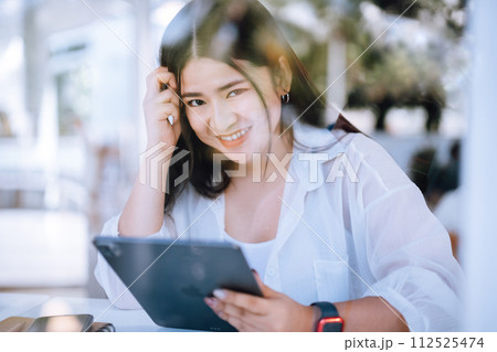 asian freelance people business female wearing smartwatch talking making using casual working with tablet for browsing internet, chatting and blogging and smartphone,notebook in coffee shop. 112525474