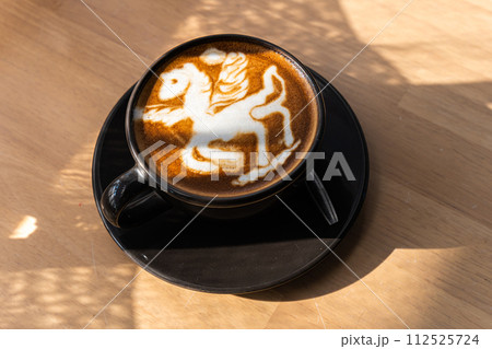 Hot coffee latte with latte art in the form of a horse milk foam in cup mug on wood desk on top view. As breakfast In a coffee shop at the cafe,during business work concept Hot coffee latte with latte art in the form of a horse milk foam in cup mug on wood desk on top view. As breakfast In a coffee shop at the cafe,during business work concept 112525724
