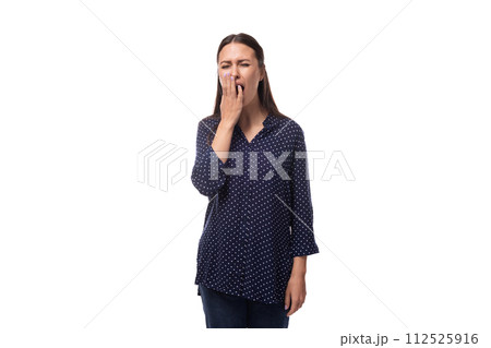 a young brunette woman dressed in a blue blouse with a pattern of peas yawns from longing 112525916