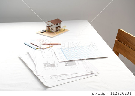 窓際の白いテーブルの置かれた住宅設計図と住宅模型 窓際の白いテーブルの置かれた住宅設計図と住宅模型 112526231