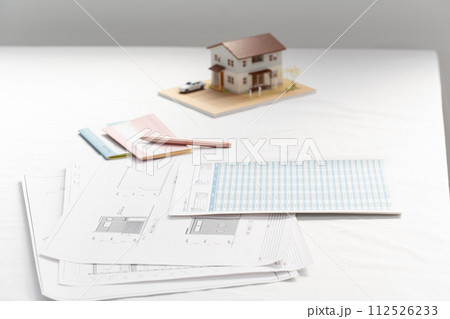 窓際の白いテーブルの置かれた住宅設計図と住宅模型 窓際の白いテーブルの置かれた住宅設計図と住宅模型 112526233