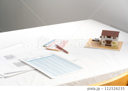 窓際の白いテーブルの置かれた住宅設計図と住宅模型 112526235