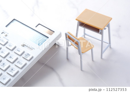 学校の机と椅子、電卓がイメージする、高騰を続けて家計を圧迫する教育費のイメージ 学校の机と椅子、電卓がイメージする、高騰を続けて家計を圧迫する教育費のイメージ 112527353
