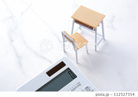 学校の机と椅子、電卓がイメージする、高騰を続けて家計を圧迫する教育費のイメージ 学校の机と椅子、電卓がイメージする、高騰を続けて家計を圧迫する教育費のイメージ 112527354