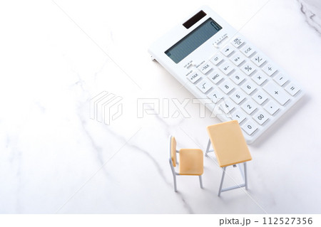 学校の机と椅子、電卓がイメージする、高騰を続けて家計を圧迫する教育費のイメージ 学校の机と椅子、電卓がイメージする、高騰を続けて家計を圧迫する教育費のイメージ 112527356
