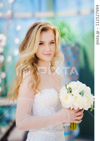 Beautiful blonde bride in a tight-fitting dress with a bouquet.  112527984