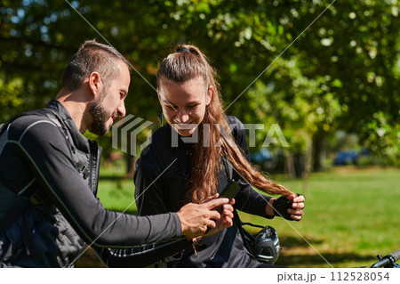 A sweet couple, equipped with bicycles and engrossed in coordinating their journey, checks their GPS mobile and watches while planning scenic routes in the park, seamlessly blending technology and A sweet couple, equipped with bicycles and engrossed in coordinating their journey, checks their GPS mobile and watches while planning scenic routes in the park, seamlessly blending technology and 112528054