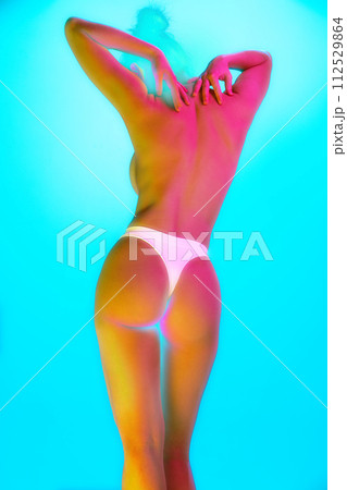 Rear view portrait of young woman posing raising hands in neon light against gradient background. Back, buttocks. Rear view portrait of young woman posing raising hands in neon light against gradient background. Back, buttocks. 112529864