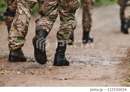Close up photo, the resilient legs of elite soldiers, clad in camouflage boots, stride purposefully along a hazardous forest path as they embark on a high-stakes military mission Close up photo, the resilient legs of elite soldiers, clad in camouflage boots, stride purposefully along a hazardous forest path as they embark on a high-stakes military mission 112530034