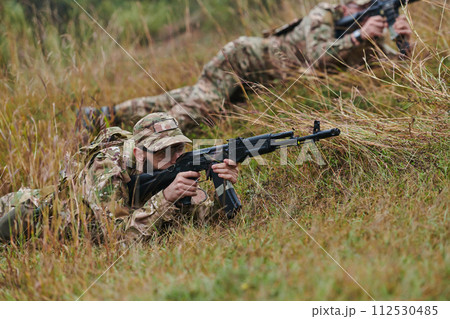 Elite soldiers stealthily maneuver through the dense forest, camouflaged in specialized gear, as they embark on a covert and strategic military mission 112530485
