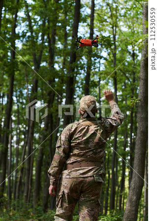 Elite military unit, equipped with state-of-the-art technology including a drone, strategically navigates and surveys dangerous wooded terrain, showcasing their precision, cooperation, and specialized 112530559