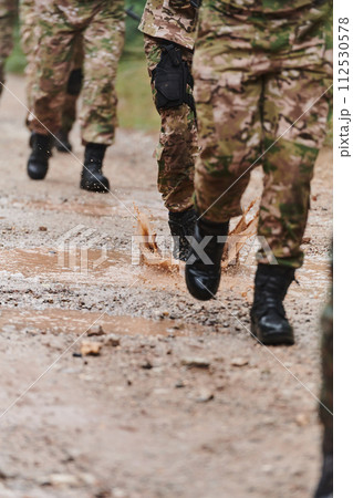 Close up photo, the resilient legs of elite soldiers, clad in camouflage boots, stride purposefully along a hazardous forest path as they embark on a high-stakes military mission 112530578