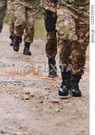 Close up photo, the resilient legs of elite soldiers, clad in camouflage boots, stride purposefully along a hazardous forest path as they embark on a high-stakes military mission 112530585