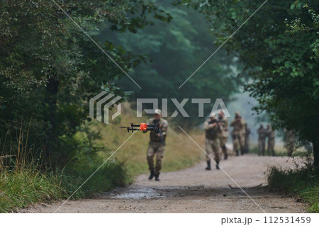 Elite military unit parading and securing the forest, utilizing drones for terrain scanning and reconnaissance, showcasing their advanced skills and specialized training in high risk operations Elite military unit parading and securing the forest, utilizing drones for terrain scanning and reconnaissance, showcasing their advanced skills and specialized training in high risk operations 112531459