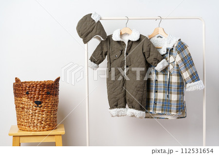 Two kids winter coats hanging on hangers against white wall 112531654