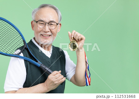 A senior male holding a tennis racket and a medal 112531668