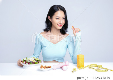 A woman holding a pill in front of her diet and exercise equipment 112531819
