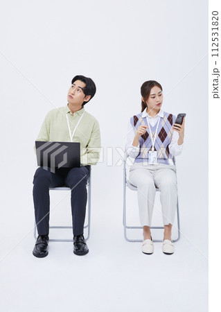 A man and a woman sitting in a chair playing a laptop and a smartphone 112531820