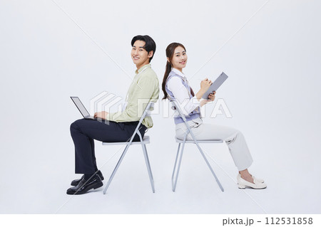 A man and a woman sitting back to back and playing a tablet with a laptop 112531858