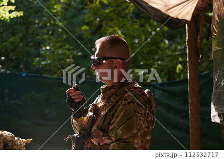 A military major employs a Motorola radio for seamless communication with his fellow soldiers during a tactical operation, showcasing professionalism and strategic coordination A military major employs a Motorola radio for seamless communication with his fellow soldiers during a tactical operation, showcasing professionalism and strategic coordination 112532717