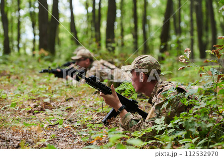 Elite soldiers stealthily maneuver through the dense forest, camouflaged in specialized gear, as they embark on a covert and strategic military mission 112532970