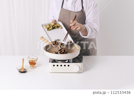 A woman is putting mushrooms soaked in a frying pan with chopsticks A woman is putting mushrooms soaked in a frying pan with chopsticks 112533436